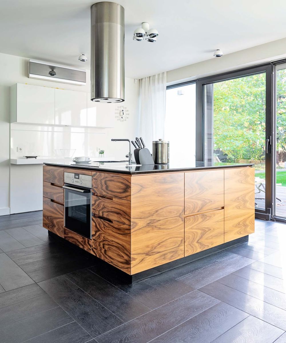 Modern kitchen interior with wooden kitchen island with oven and window in the room. Design indoors architecture and luxury in new apartment with tiled floor. Vertical.